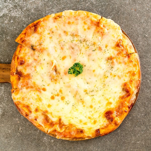 A whole Italian four cheese pizza with a sprig of parsley on a wooden paddle.