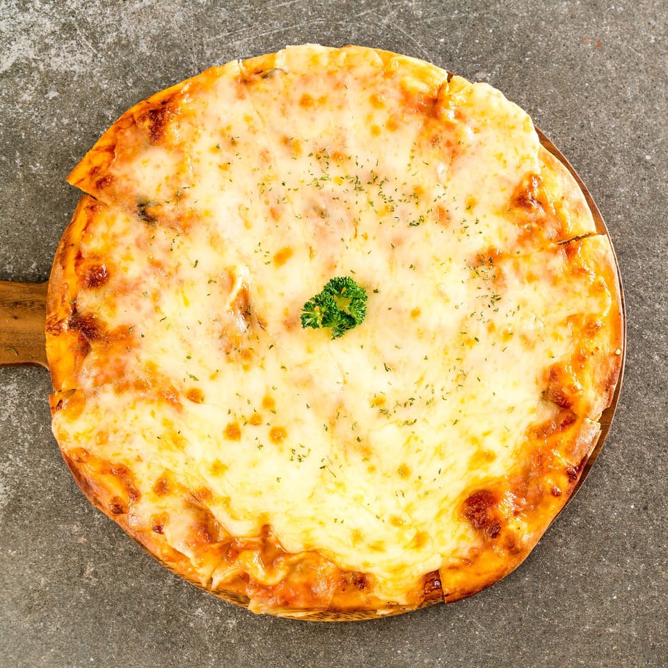 A whole Italian four cheese pizza with a sprig of parsley on a wooden paddle.