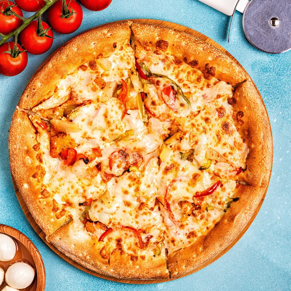 A freshly baked Italian pizza with melted cheese, red peppers, and pineapple, on a wooden board.