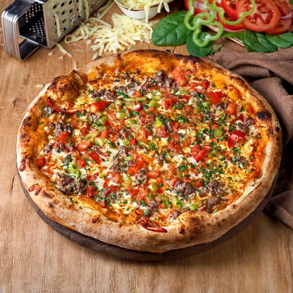 A delicious Italian pizza from The Village, topped with ground meat, diced tomatoes, and green peppers.