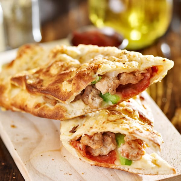 Two halves of a golden-brown calzone filled with sausage, green peppers, and cheese on a wooden board.