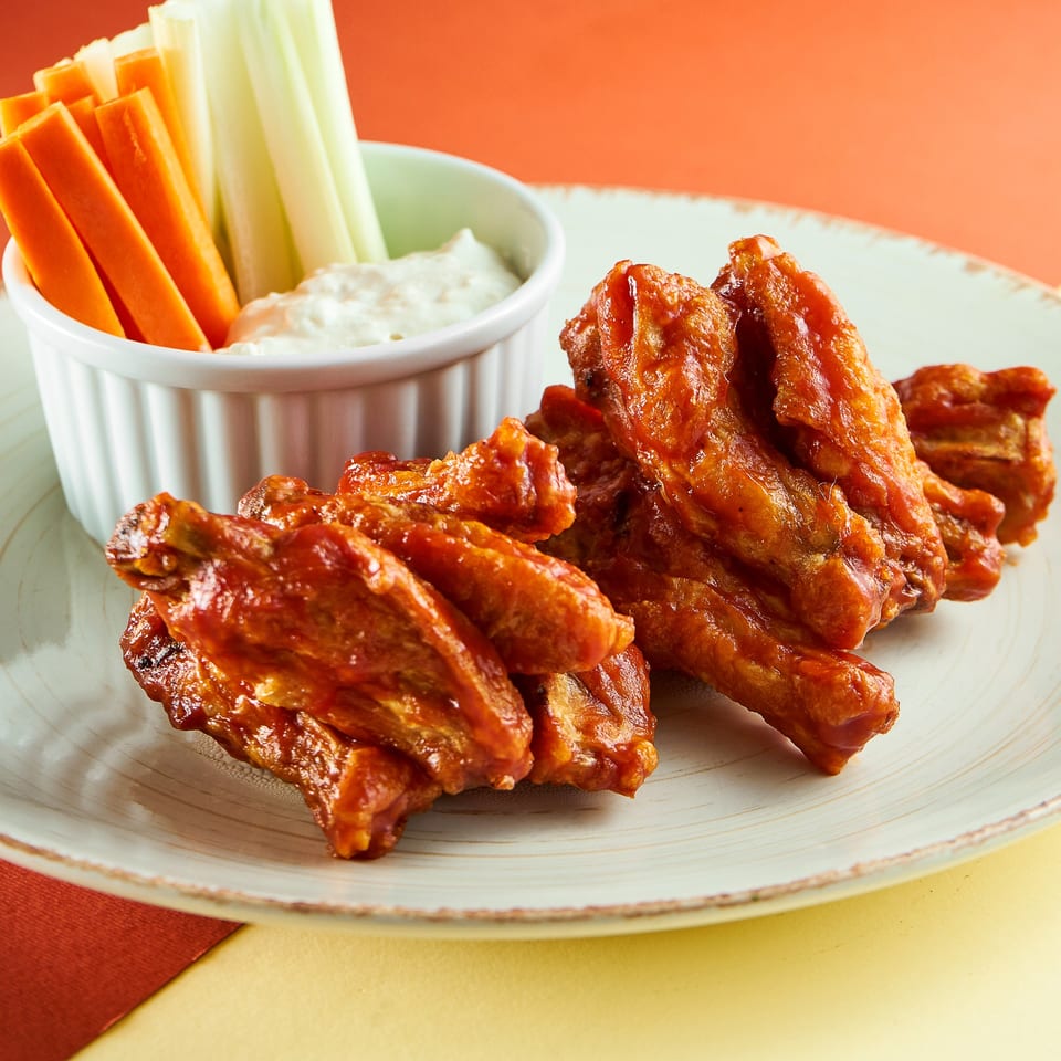 Spicy chicken wings with celery and carrot sticks, and a side of creamy dip.